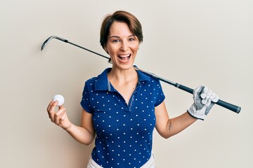 Young brunette woman with short hair holding ball and golf club smiling and laughing hard out loud because funny crazy joke.