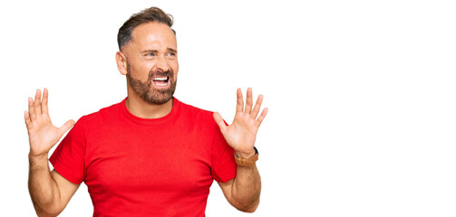 Wall Mural - Handsome middle age man wearing casual red tshirt crazy and mad shouting and yelling with aggressive expression and arms raised. frustration concept.