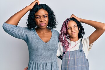 Canvas Print - Beautiful african american mother and daughter wearing casual clothes and hugging confuse and wondering about question. uncertain with doubt, thinking with hand on head. pensive concept.