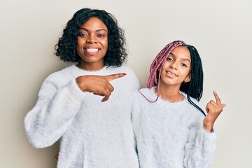 Sticker - Beautiful african american mother and daughter wearing casual winter sweater cheerful with a smile on face pointing with hand and finger up to the side with happy and natural expression