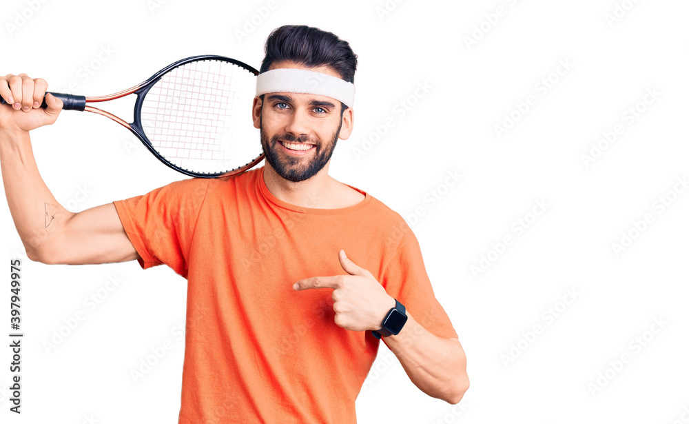 Young handsome man with beard playing tennis holding racket pointing finger to one self smiling happy and proud