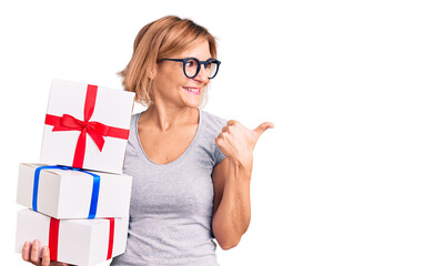 Canvas Print - Young blonde woman wearing glasses holding gift pointing thumb up to the side smiling happy with open mouth