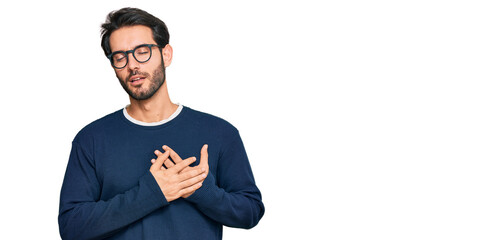 Wall Mural - Young hispanic man wearing casual clothes and glasses smiling with hands on chest with closed eyes and grateful gesture on face. health concept.