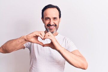 Sticker - Middle age handsome man wearing casual t-shirt standing over isolated white background smiling in love doing heart symbol shape with hands. Romantic concept.