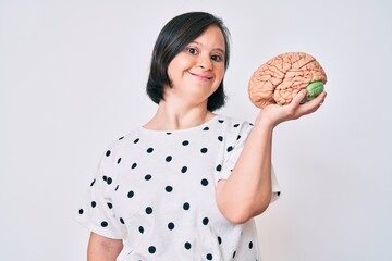 Canvas Print - Brunette woman with down syndrome holding brain looking positive and happy standing and smiling with a confident smile showing teeth