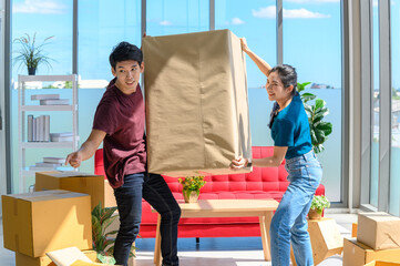 young asian couple smiling and enjoy when they carrying big cardboard box while relocation into new home on moving day, celebrating moving to new home concept