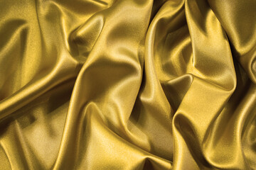 Wall Mural - Golden silk satin fabric background. Luxurious background for your design with copy space. Liquid wave or wavy folds. Close-up.