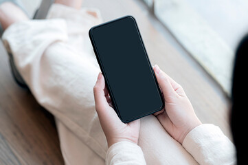 Wall Mural - closeup image of woman hands holding blank screen smartphone while sitting on the floor at home.