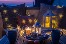 Cozy Sitting Area With Coffee And Cookies On A Balcony, Decorated For Winter With Lanterns, Candles, Woolen Blankets And Fairy Lights In Beautiful Sundown Light