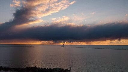 Wall Mural - Beautiful sunset aerial panning over breakwater rocks with the white colored Ludington breakwater lighthouse sitting on the horizon in front of a beautiful orange and blue cloud sky on Lake Michigan.
