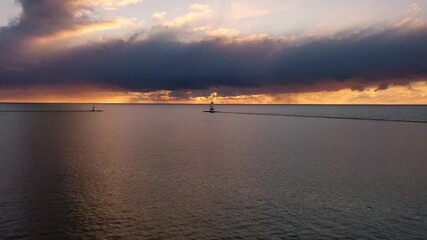 Wall Mural - Beautiful sunset aerial pull out or panning back view of the white colored Ludington breakwater lighthouse with blue and orange sky and clouds above reflecting on the calm water of Lake Michigan.