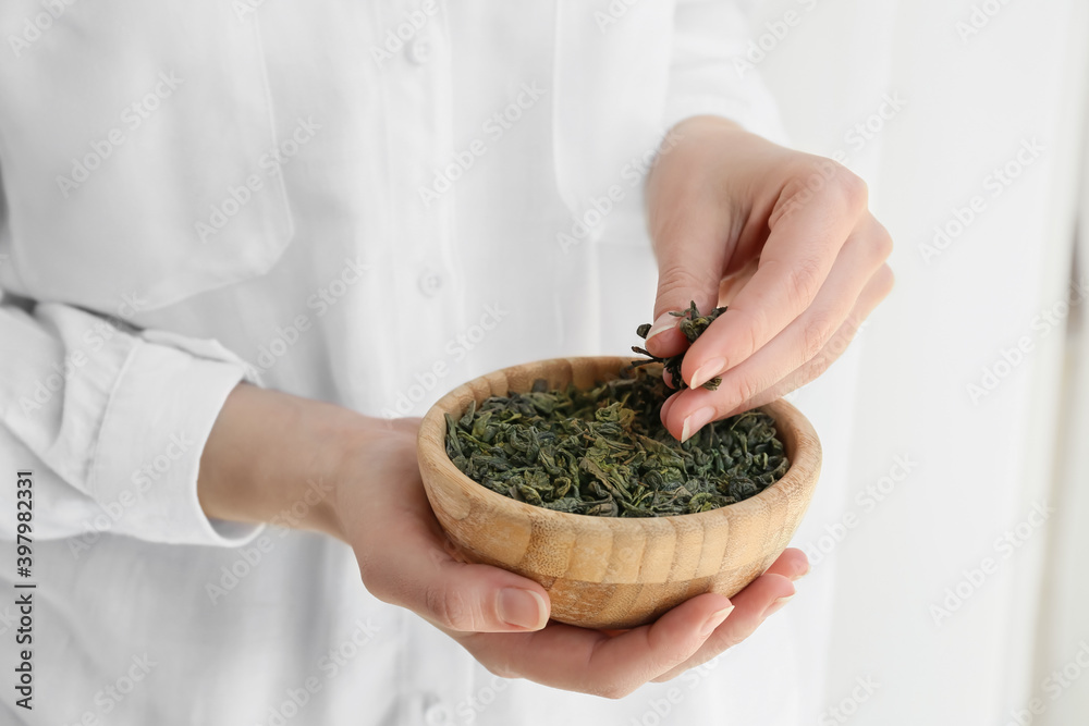 Woman with dry tea leaves in bowl, closeup
