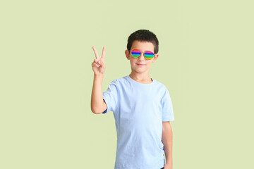 Cute boy with stylish sunglasses showing victory gesture against color background