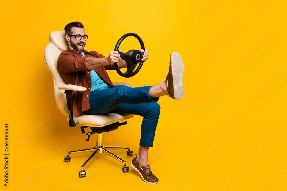 Full length body photo of happy fooling man in chair keeping steering wheel pretending car driver isolated vivid yellow color background - obrazy, fototapety, plakaty 