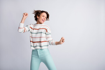 Photo of funny charming young woman dressed striped pullover dancing rising fists empty space isolated grey color background