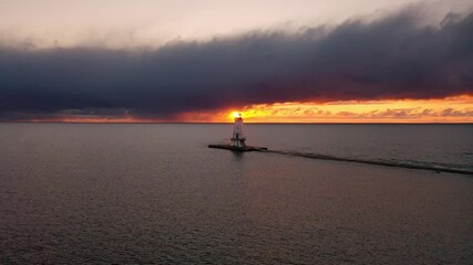 Wall Mural - Beautiful panning aerial of the Ludington Breakwater Lighthouse with the bright orange and yellow sun shining behind the structure, reflecting on the water and lighting up the clouds in sky at sunset.