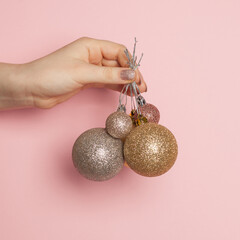 Wall Mural - Shiny Christmas balls decoration in woman hand on pastel pink card background