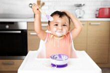 Messy Baby In High Chair Eating Yogurt And Raising Hands