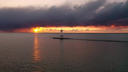 Wall Mural - Beautiful aerial sunset view of the Ludington Breakwater Lighthouse as the bright yellow and orange sun lights up the sky and clouds and reflects and shimmers on the calm water of Lake Michigan.