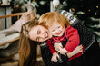 © Serhii - Merry Christmas and Happy Holidays. Cheerful mom hugging cute baby daughter girl near Christmas tree. Mother and little child having fun and playing together at home. Close up.