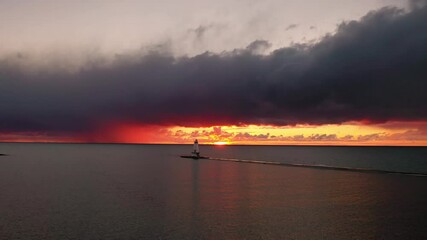 Wall Mural - Beautiful panning out aerial of the Ludington Breakwater Lighthouse with the sun reflecting on the water of Lake Michigan and lighting up the sky and clouds with colorful pink, orange and yellow.