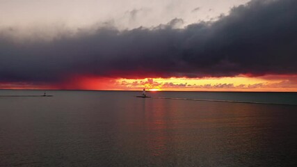 Wall Mural - Beautiful panning out aerial of the Ludington Breakwater Lighthouse with the sun reflecting on the water of Lake Michigan and lighting up the sky and clouds with colorful pink, orange and yellow.