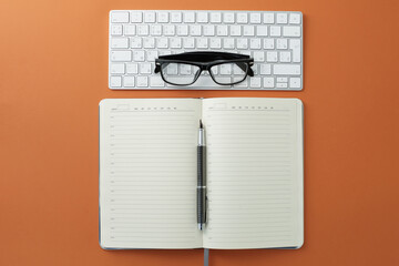 Glasses keyboard mouse pen and diary on orange background