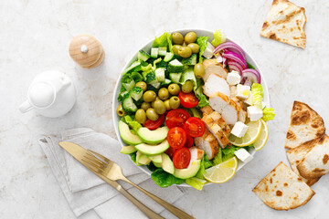 Canvas Print - Greek inspired salad with grilled chicken meat, vegetables and feta cheese in a bowl on a table, with olive oil dressing, top view