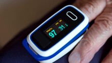 Digital pulse oximeter on old person's finger, blinking device monitor showing oxygen rate index. Senior man measuring oxygen in blood, cardiology examination of elderly person