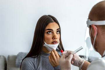 Wall Mural - Shot of a male doctor in protective suit taking swab test from young female patient.Medical worker in protective suit taking a swab for corona virus test.Coronavirus through testing with young women.