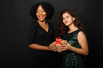 Wall Mural - Indoor portrait of two happy best friends sisters women, ready for holiday party, holding bright gifts and presents, wearing bright dresses