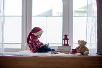 Canvas Print - Sweet blonde child, boy, sitting on window shield with teddy bear friend toy, writing letter to Santa Claus and reading book