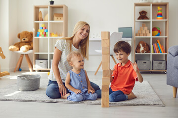 mom with two small children have fun playing assembling a tower of wooden eco cubes at home.