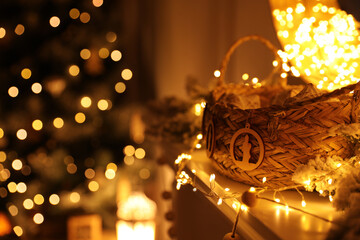 Poster - Fireplace mantel with wicker basket, festive lights and blurred Christmas tree on background