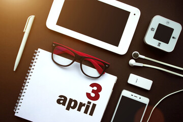 April 3rd. Day 3 of month, Calendar date. Office workplace with laptop, notebook, office supplies and stationery on brown back. Spring month, day of the year concept.