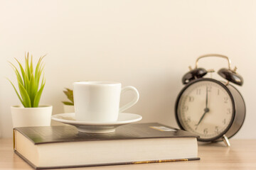 A small Cup of morning coffee, an alarm clock, and a book on the table.