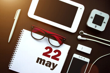 May 22nd. Day 22 of month, Calendar date. Office workplace with laptop, notebook, office supplies and stationery on brown back. Spring month, day of the year concept.