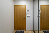 Fototapeta Tulipany - Modern interior of entrance hall in apartment. Front view of wooden door. White wall. Mirror sliding door wardrobe.