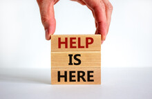 Help Is Here Symbol. Male Hand Builds Stack From Blocks With Words 'here To Help'. White Table. Beautiful White Background. Copy Space. Business And Help Is Here Concept.