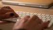 © Luis - Persona haciendo teletrabajo desde casa, con las manos tecleando letras del teclado. Al fondo,  una mesa de madera   .