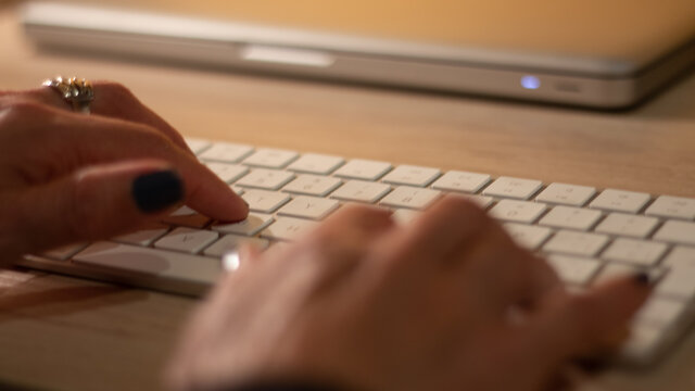 Persona haciendo teletrabajo desde casa, con las manos tecleando letras del teclado. Al fondo,  una mesa de madera   .