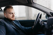 © velimir - male driver in business clothes and glasses drives a car in winter.