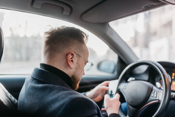 Wall Mural - male driver in business clothes typing in a smartphone in a car