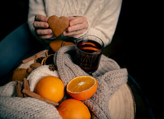 warm drinks in cold weather, a girl with a glass of gluntwine and heart-shaped cookies, on the table oranges, cookies and spices