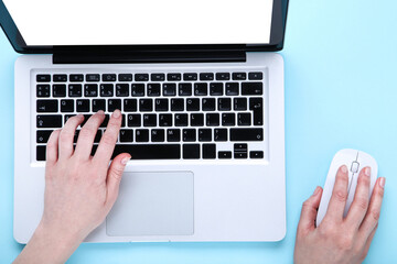 Poster - Female hands typing on laptop keyboard and using mouse on blue background