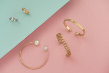 Golden Jewelries Bracelets And Rings On Pink And Blue Background