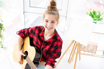 Wall Mural - Happy teenage girl playing guitar in bright room