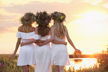 Wall Mural - Young women wearing wreaths made of flowers outdoors at sunset, back view