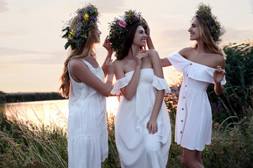 Wall Mural - Young women wearing wreaths made of beautiful flowers outdoors at sunset