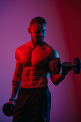 Wall Mural - A muscular man with a beard who is doing bicep curls with dumbbells under blue and red lights. An athletic guy is demonstrating his sporty physique. A smiling athlete is training his arms hard.